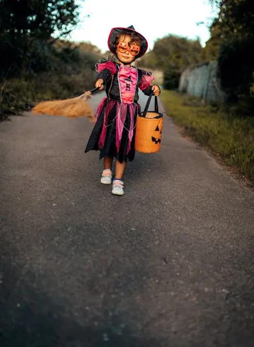 Little girl masquerade as a witch with halloween lantern and broom