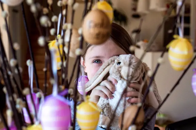 Girl hiding behind Easter bunny and twigs of pussy willows decorated with Easter eggs