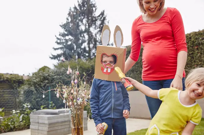 Pregnant mother with boy wearing bunny mask and happy girl in garden