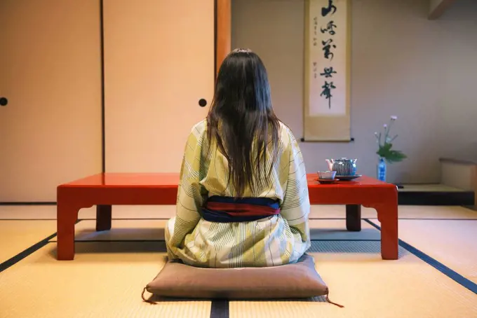 Japan, Uji, back view of woman wearing yukata drinking tea in a traditional Japanese room