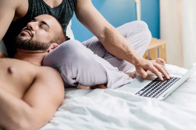 Gay couple lying in bed, using laptop