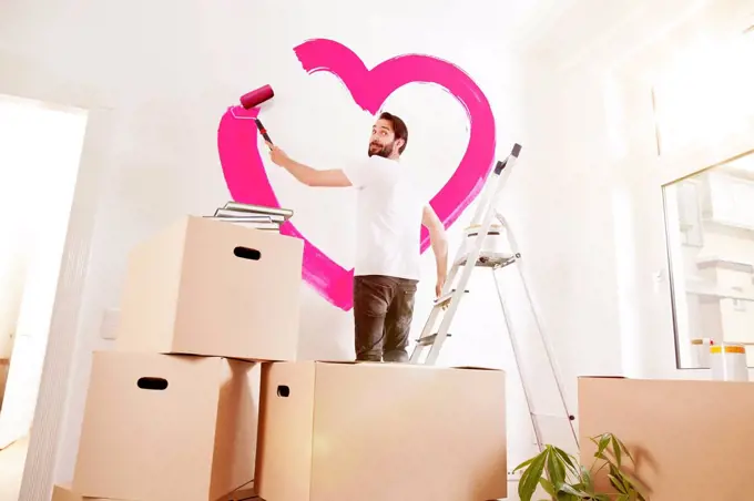 Young man painting a pink heart on a wall in new apartment