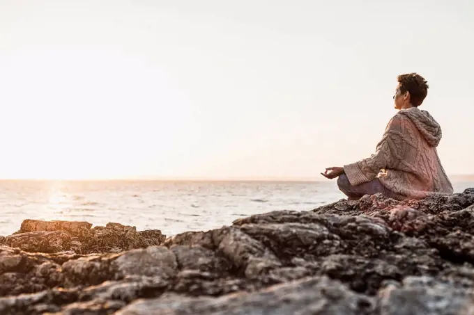France, Crozon peninsula, woman meditating at beach at sunset