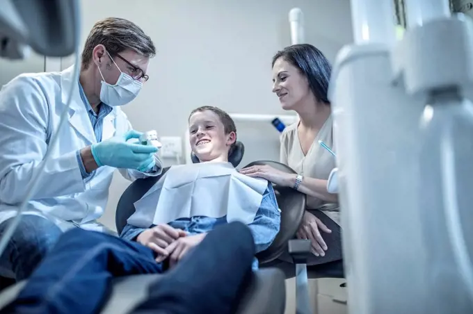 Orthodontist explaining dental mold to boy with mother in dental surgery
