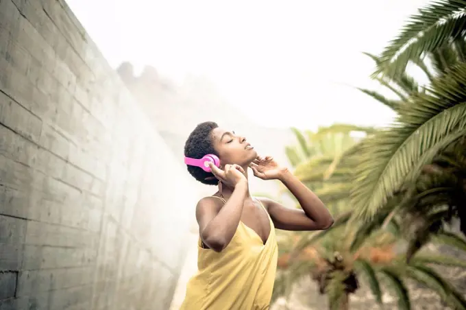 Spain, woman with eyes closed listening music with pink headphones