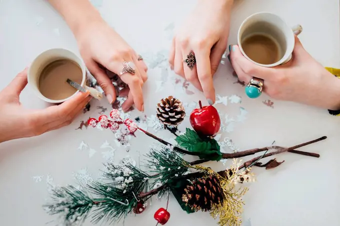 Hands of two women holding cups of coffee on a tabletop with Christmas decoration