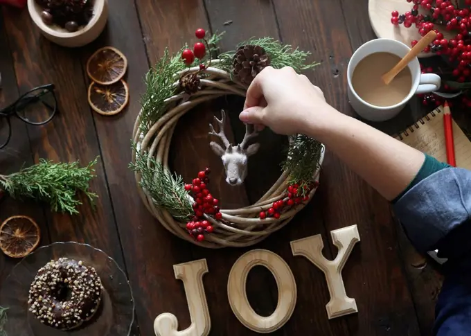 Woman's hand decorating Christmas wreath on wooden table