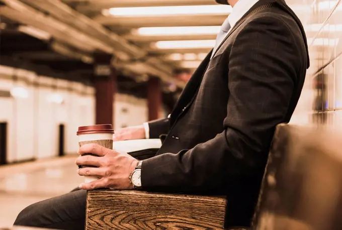 Young businessman waiting at metro station platform, holding disposable cup