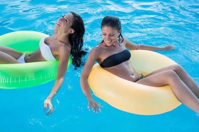 Two young women floating on water in swimming pool