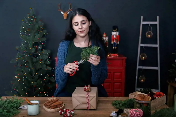Young woman cutting twig for decorating Christmas present