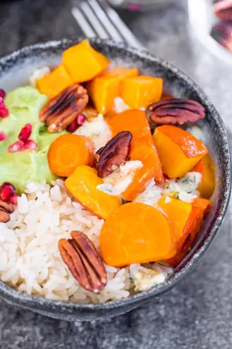 Bowl of autumnal salad with carrots, pumpkin, sweet potatoes, pecan, guacamole, pomegranate and rice