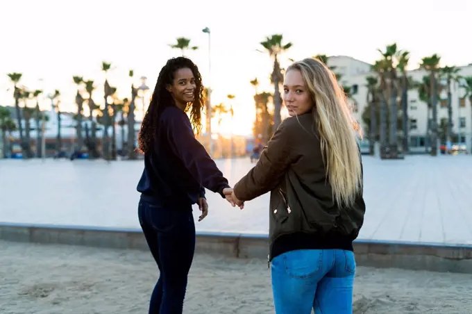 Two young women walking hand in hand at sunset