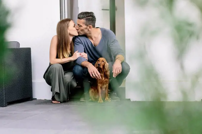 Couple with dog kissing at terrace door