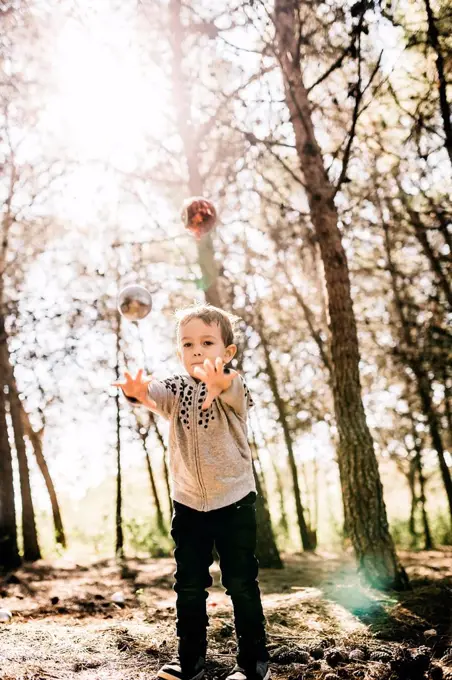 Little boy standing in the woods throwing Christmas baubles in the air