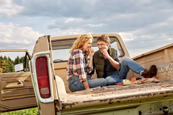 Couple sitting on pick up truck having a picnic