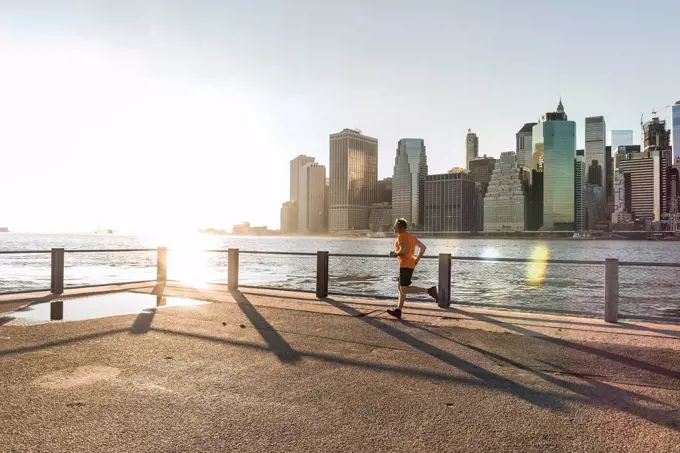 USA, Brooklyn, man jogging in front of Manhattan skyline in the evening