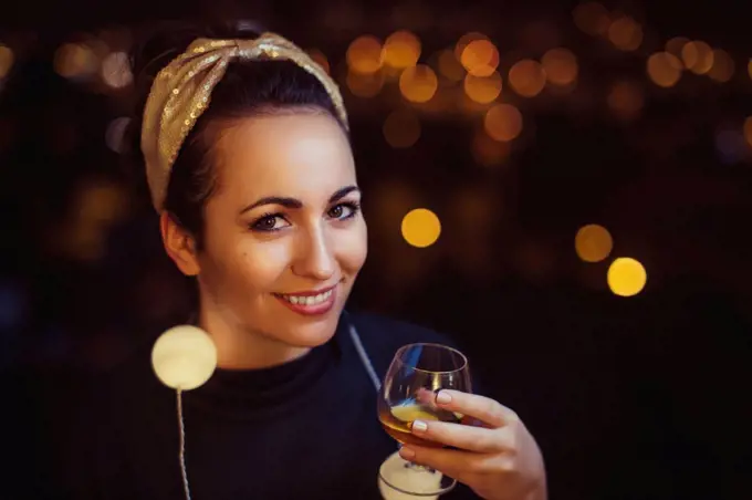 Portrait of smiling woman with drink wearing golden hair-band