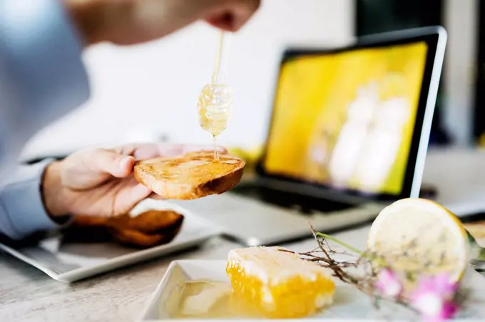 Woman dripping honey on toast at his workplace, close-up