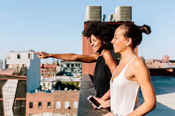 Female friends standing on rooftop, pointing at distance