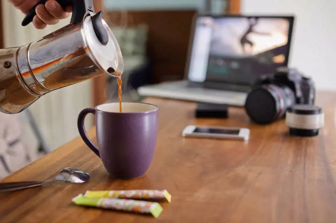 Photographer pouring coffee into cup at desk at home