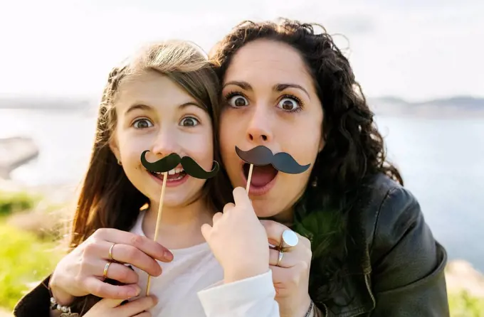 Mother and daughter having fun holding fake moustaches