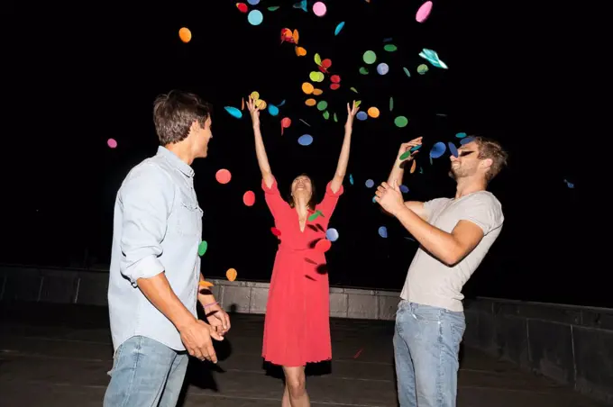 Young people having a rooftop party, throwing confetti
