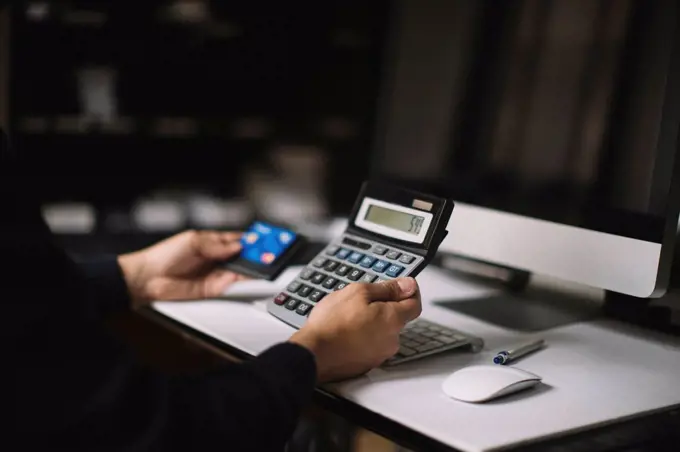 Man using calculator and credit card at desk, partial view