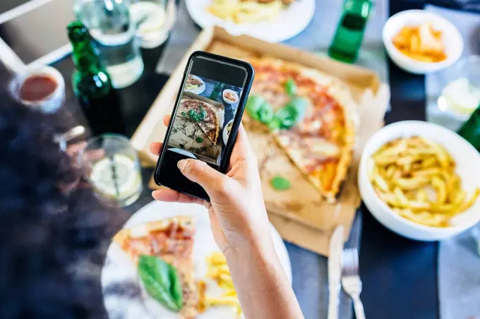 Hand taking cell phone picture of pizza on table