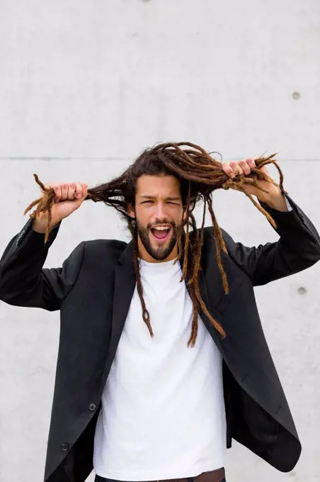 Portrait of young businessman with dreadlocks pulling funny faces