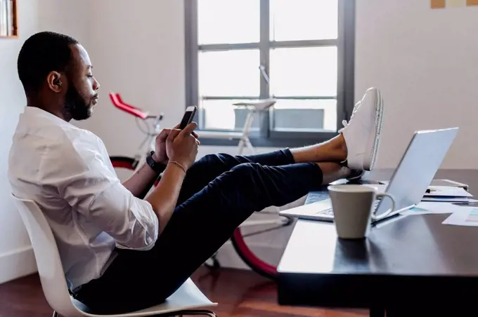 Man using cell phone in home office with feet on desk