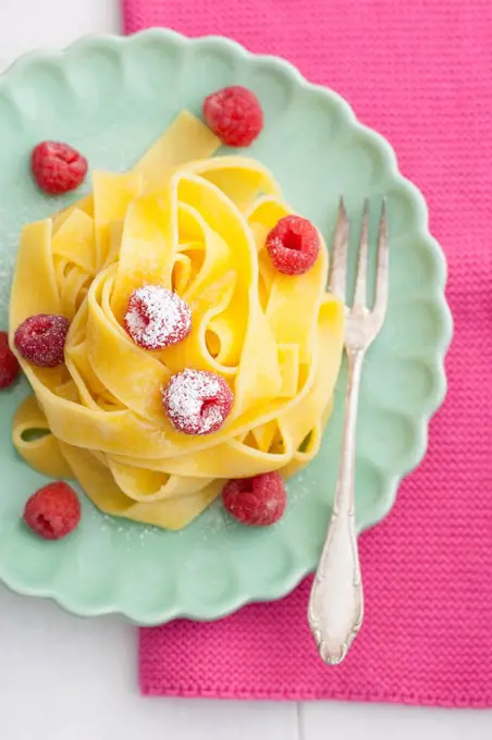 Homemade fettuccine with raspberries on plate, close up