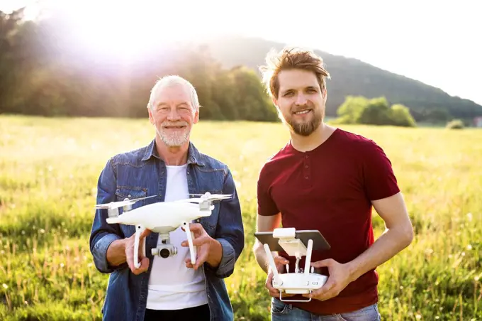 Portrait of senior father and his adult son with drone on a meadow