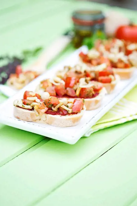 Plate of bruschetta with tomatoes, white shimeji mushrooms, herbs and olive oil on wooden table, close up