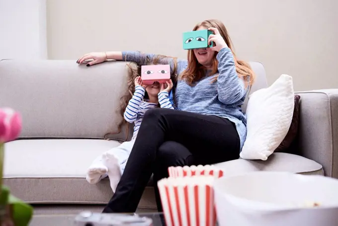 Mother and little daughter sitting on the couch having fun with Virtual Reality Glasses