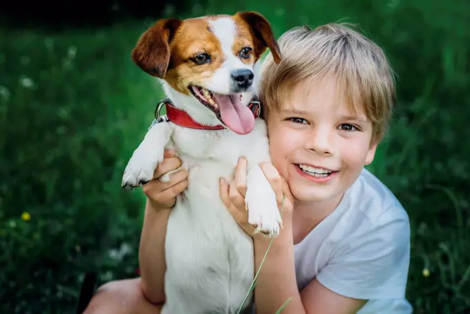 Portrait of happy little boy with his dog on meadow in the garden