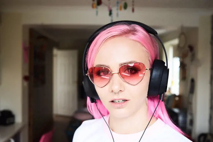 Portrait of young woman with pink hair and heart-shaped sunglasses listening to music