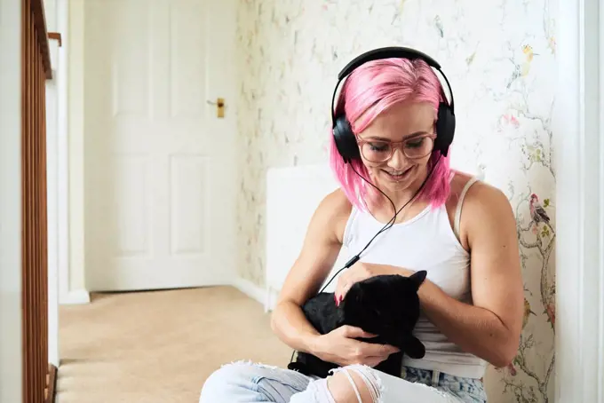 Happy young woman with black cat listening to music at home