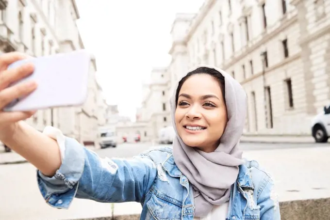 UK, England, London, young woman wearing hijab taking a selfie in the city