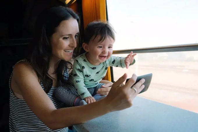 Happy mother and baby girl using smartphone while traveling by train
