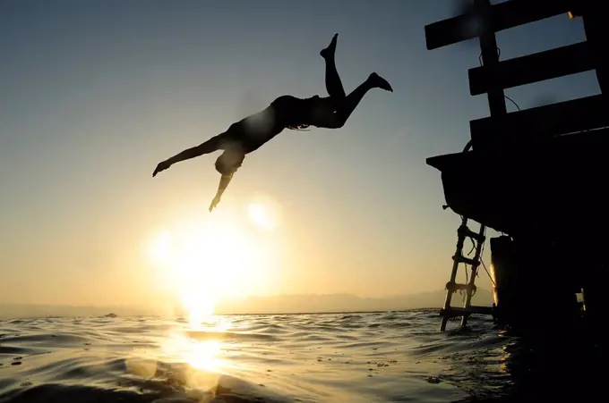 Man jumping fom jetty into the sea at sunset