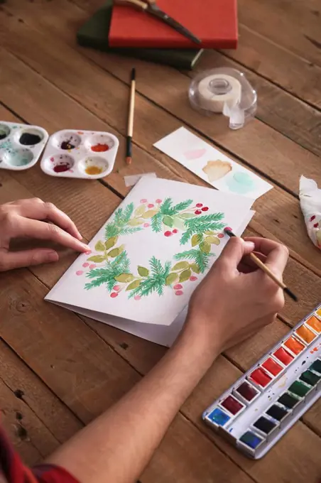 Young woman painting Christmas card with water colors, close-up