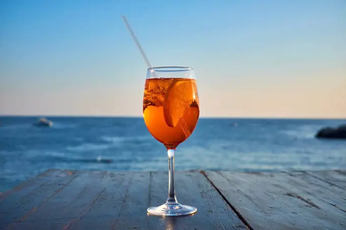 Glass of ice-cooled Spritz with orange slice in front of the sea