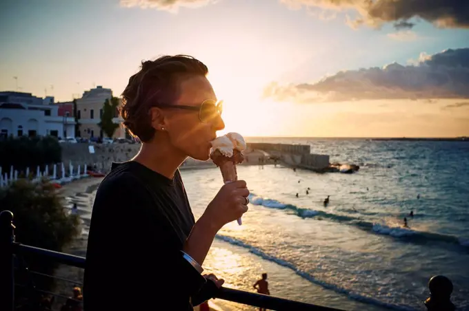 Italy, Santa Maria al Bagno, woman eating ice cream cone at backlight