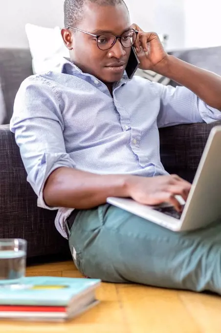 Young man on the phone sitting on the floor in the living room using laptop