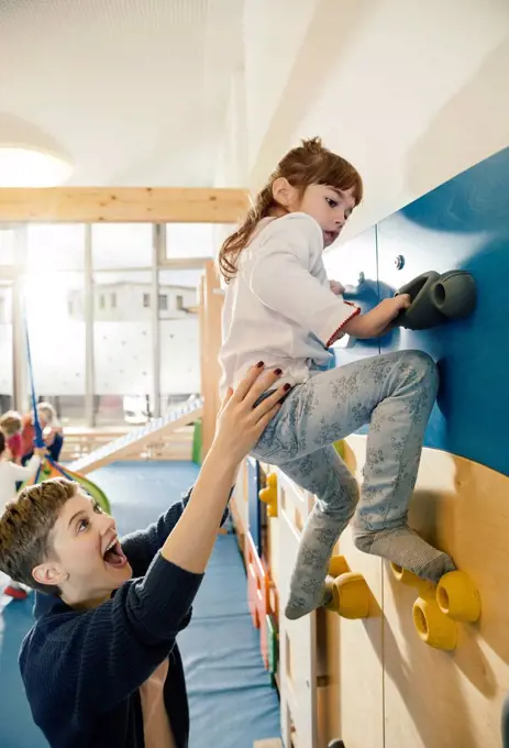 Pre-school teacher helping little girl climbing up a wall