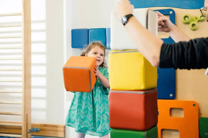 Happy little girl lifting up a soft building block in gym room of a kindergarten