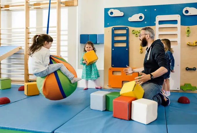 Pre-school teacher and happy children playing in gym room in kindergarten