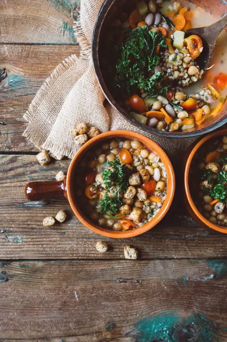 Mediterranean soup in copper pot and terracotta bowls on wood