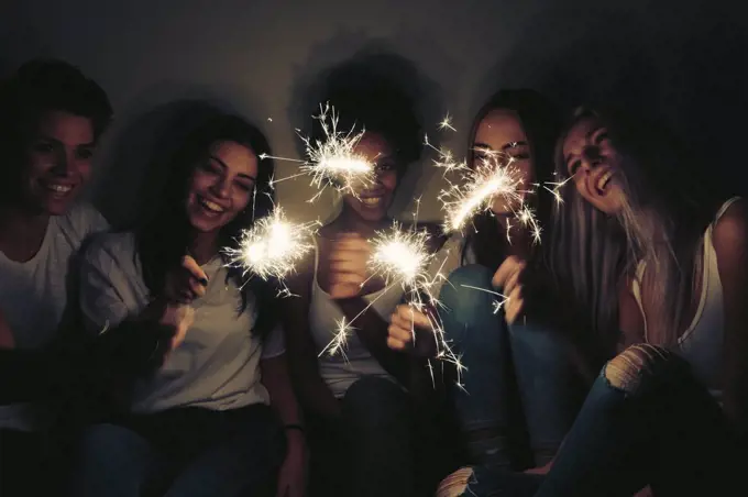 Happy female friends with sparklers in the dark