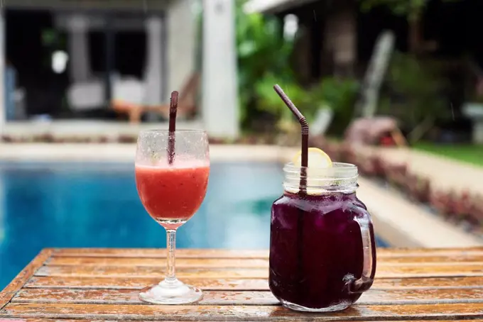 Two fruity cocktails at the poolside in rain